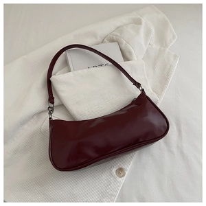 Détail du sac à main bordeaux brillant sur une veste en velours blanc et livre d'art