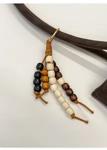 Detailed view of Chinese style wooden beaded charm with gold ring on a suede tote bag