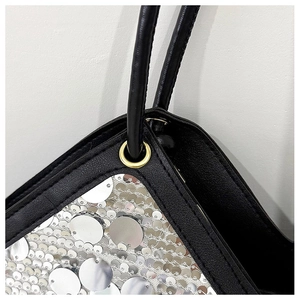 Detail of black leather tote with shimmering silver sequins and golden metal ring accents