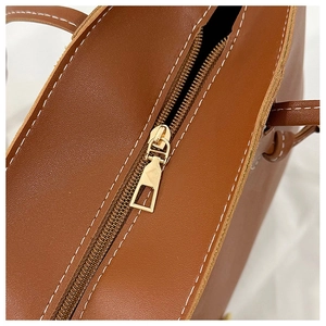 Detail of golden zipper and contrast white stitching on a brown leather tote bag