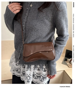 Detail of a brown patent leather crossbody bag with wave-edge flap on a model