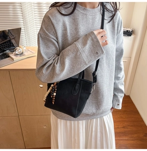 Detail of minimalist black matte bucket bag with colorful wooden bead charm and strap