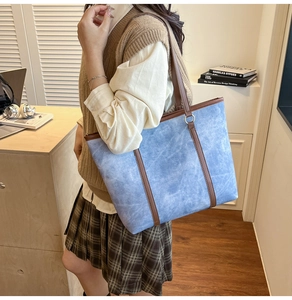Blue denim tote bag with brown leather straps shown in a cozy home office setting