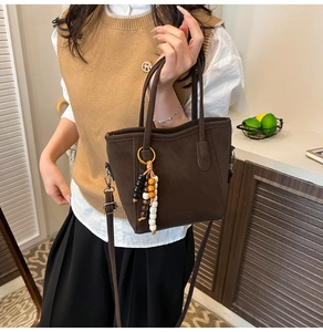 Macro detail of dark brown suede bucket bag with vintage wooden bead charm and crossbody strap