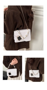 Detail of white square crossbody bag with gold chain handle and black metal plaque