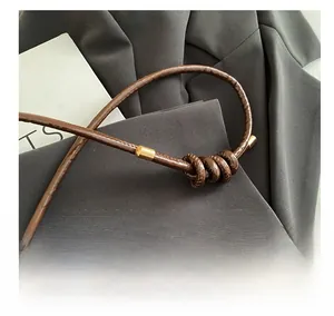 Detail of a brown glossy leather shoulder strap featuring an elegant knot and gold metal tips