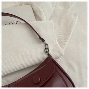 Detail of dark red glossy leather handbag featuring metal chain link and buckle craftsmanship