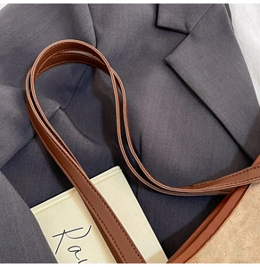 Detail of brown leather straps with precise stitching on a beige canvas tote bag