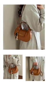 Brown leather half-moon shoulder bag with adjustable strap and beaded pendant detail
