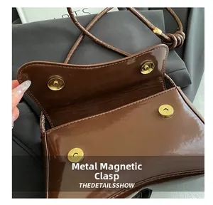 Detail of golden magnetic closure on a brown glossy leather shoulder bag