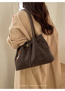 Macro view of dark brown faux suede tote bag featuring gold buckle and beaded tassel detail