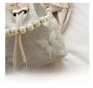 Détail du sac seau en dentelle crème avec papillon 3D, poignée en perles et cordon