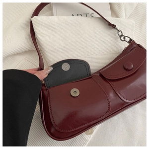 Detail of magnetic snap closure and glossy faux leather texture on burgundy shoulder bag