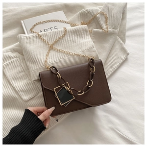 Detail of dark brown matte leather bag with dual geometric metal buckles and golden chain