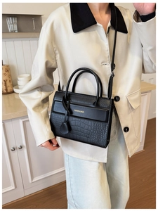 Close-up of black crocodile embossed faux leather bag with gold lettering and dual handles
