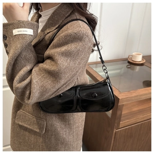 Detail of glossy black patent leather underarm bag featuring dual front buckle pockets