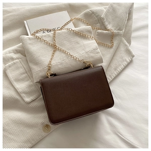 Detail of dark brown matte leather bag on corduroy jacket with golden chain strap