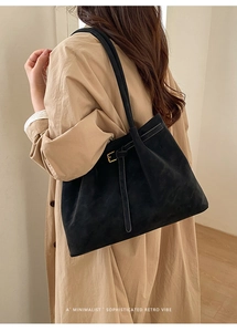 Detail of a black matte suede tote bag with slim shoulder straps and gold hardware