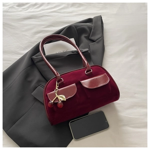 Detail of burgundy velvet shoulder bag with dual pockets and cherry metal charm accessory