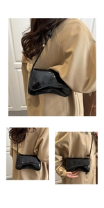Detail shot of black patent leather underarm bag with unique curved flap and glossy finish