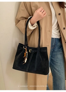 Detail of black suede tote bag with golden E-buckle and colorful beaded tassel charm
