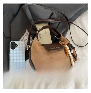 Dettaglio borsa in pelle satinata marrone con logo dorato e ciondolo con nappine in legno