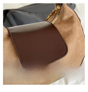 Dettaglio delle cuciture a contrasto su pelle scamosciata marrone e borsa in pelle