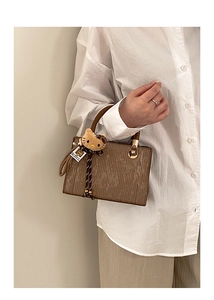 Détail du sac bandoulière marron texturé avec fermoir doré et pendentif en peluche