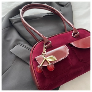Detail view of burgundy velvet baguette bag with cherry charm on a grey blazer background
