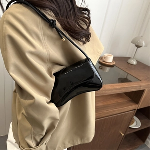 Glossy black patent leather underarm bag with knot detail worn by model in trench coat
