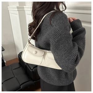 Détail d'un sac sous le bras en cuir blanc cassé avec deux poches à rabat et boutons assortis