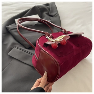 Detail of burgundy baguette bag with suede texture and cherry charm on black blazer