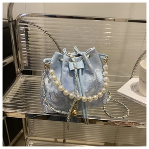 Détail du sac seau en dentelle bleu clair avec anse en perles et chaîne dorée sur étagère