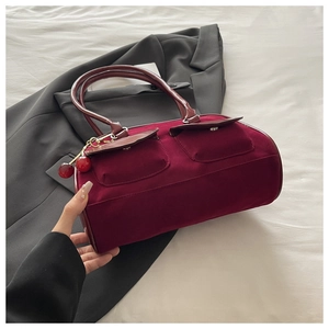 Detail of burgundy velvet shoulder bag with dual pockets and cherry charm accessory