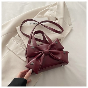 Close-up of wine red leather handbag with oversized bow and silver star rivets detailing