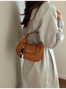 Brown suede crescent bag with gold logo and beaded tassel worn by a model