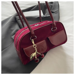 Detail of burgundy velvet handbag with patent leather pockets and gold cherry charm