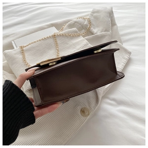 Detail view of smooth dark brown leather crossbody bag with light gold chain strap