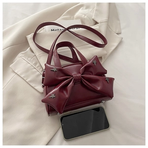 Close-up of burgundy bow handbag with star studs placed on a blazer next to a smartphone