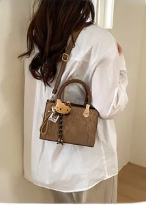 Detail view of brown pleated crossbody bag with matching plush charm on a model