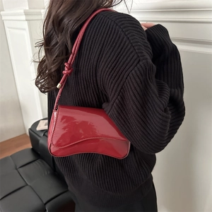 Glossy red patent leather underarm bag with unique curved design shown on shoulder