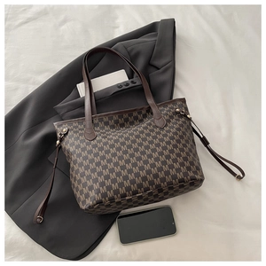 Detail view of large dark brown tote bag with repetitive M-letter monogram and slim straps