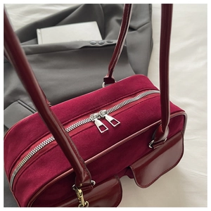 Detail of burgundy velvet handbag showing dual zipper and glossy leather pockets