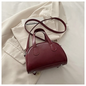 Close-up of deep red leather handbag on beige blazer with silver base protective studs