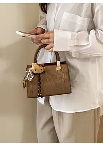 Detail of brown striped handbag featuring a golden semi-circular handle and cute charm