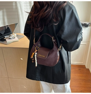 Detailed close-up of dark brown suede shoulder bag with bead charms and strap buckles