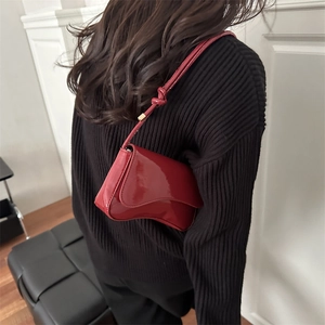 Detail of dark red patent leather baguette bag with knotted strap on model