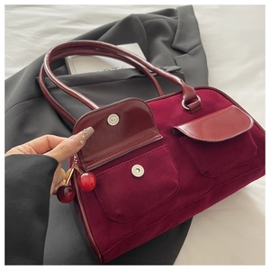 Detail of wine red suede handbag with dual pockets and decorative cherry charm