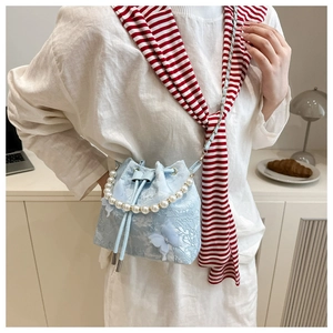 Détail d'un sac seau en dentelle bleu clair avec poignée en perles et breloque papillon