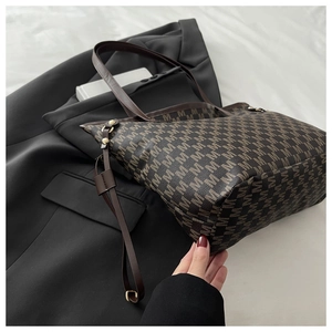 Detail of the brown tote bag with M-pattern print and gold hardware on a black blazer